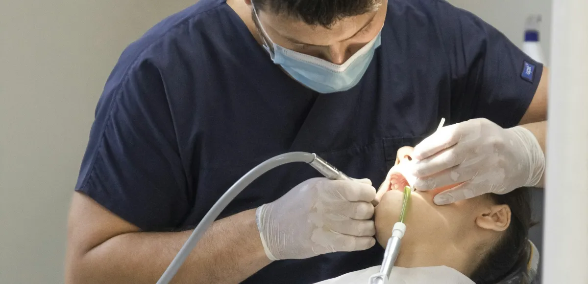 Dentista con mascarilla realizando una exploración a una paciente