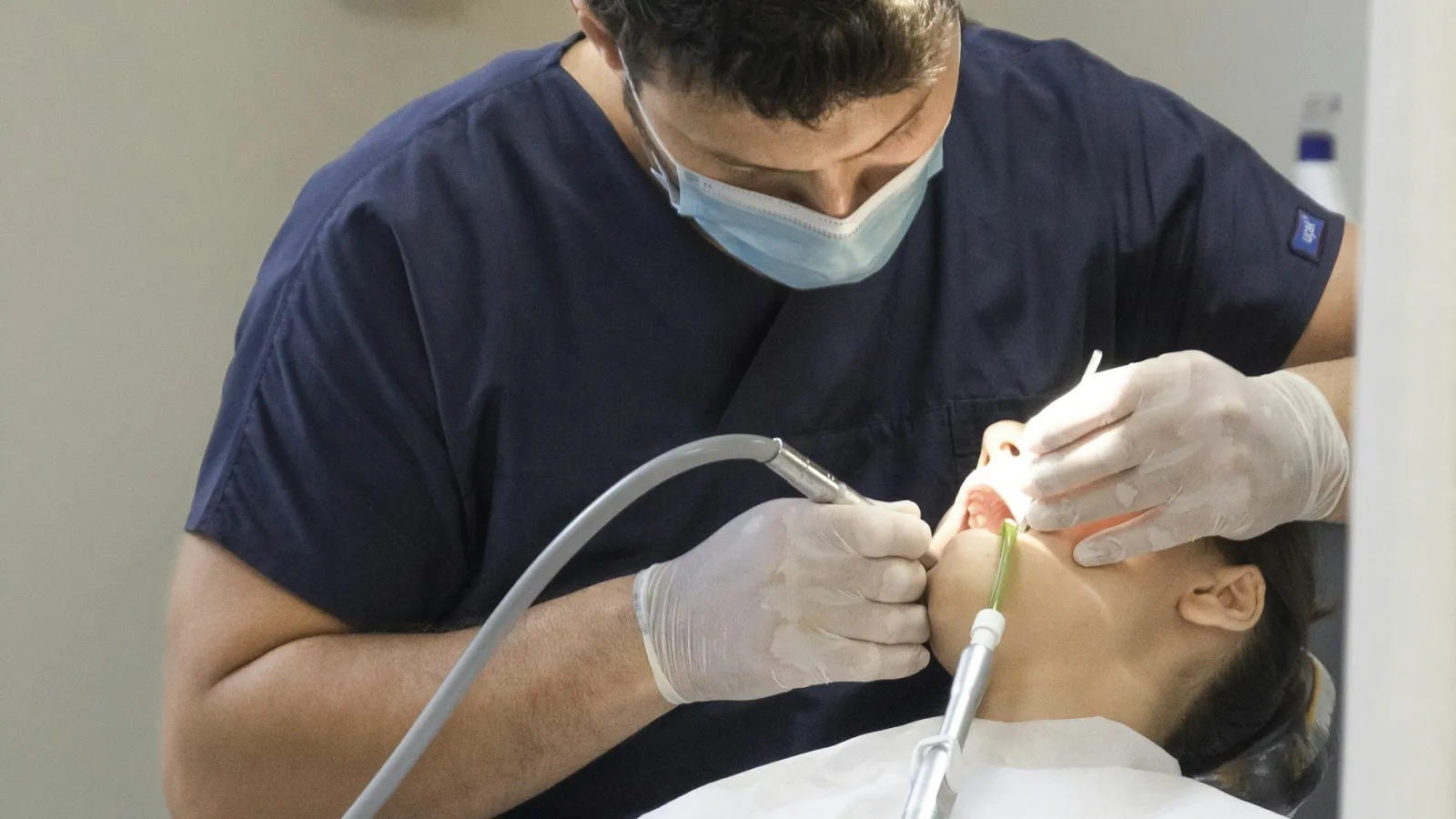 Dentista con mascarilla realizando una exploración a una paciente
